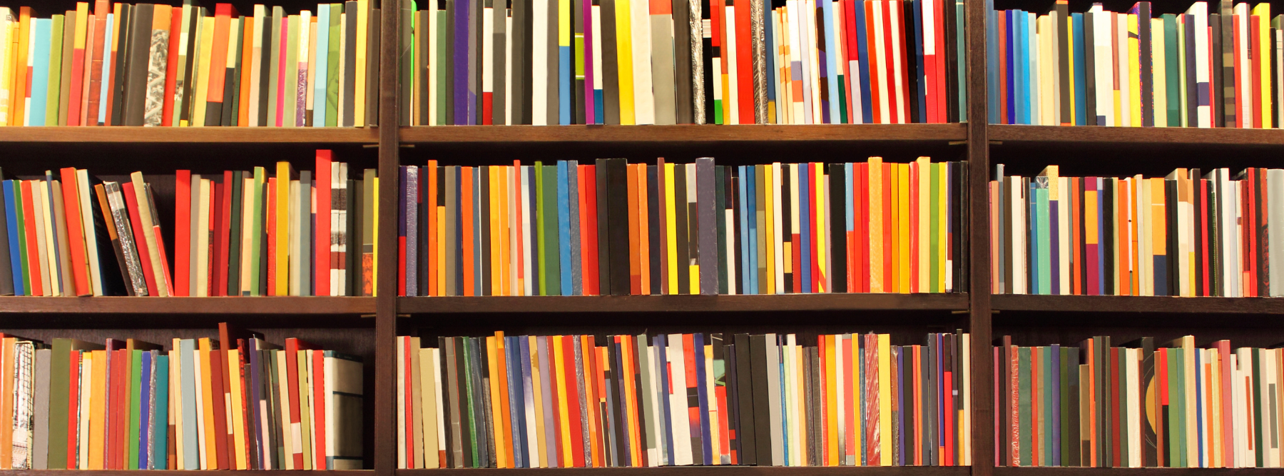 A bookshelf filled with numerous colorful books arranged vertically. The books vary in size, thickness, and color, creating a vibrant and visually striking pattern.