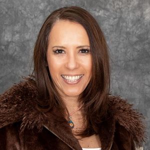 Shows Katia Marticorena, who has long brown hair and is wearing a brown jacket with a furry collar
