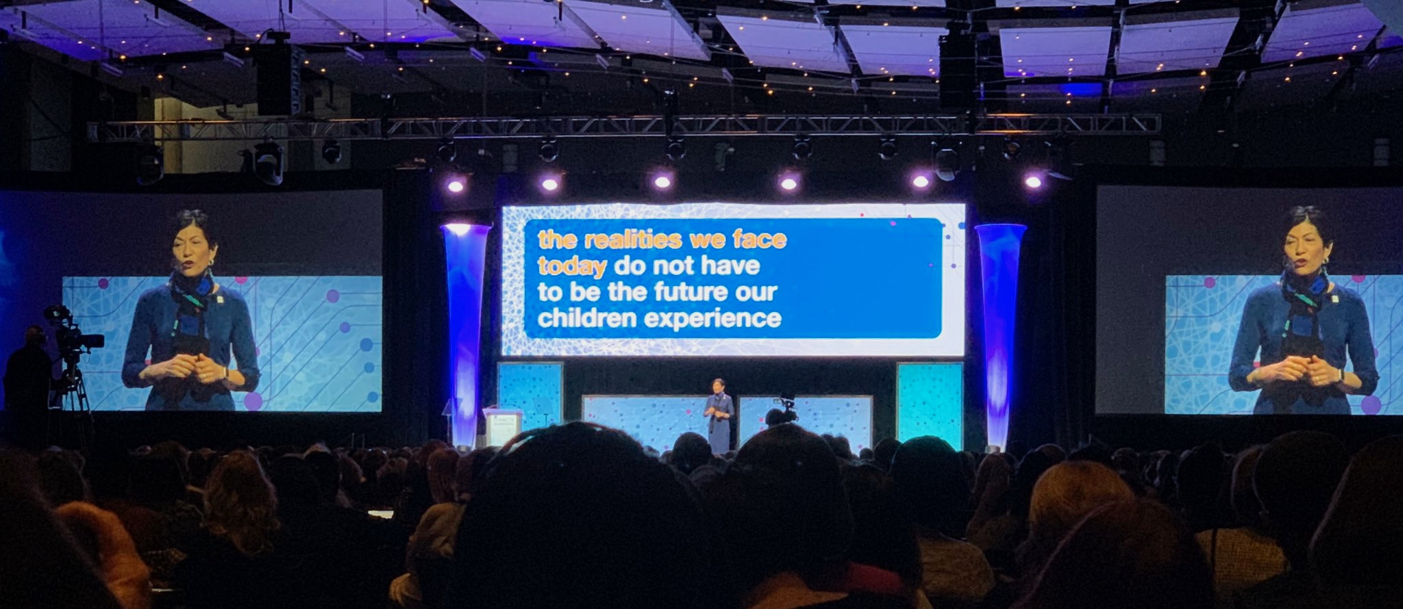 Photo of large stage with big screen that reads "the realities we face today do not have to be the future our children experience"