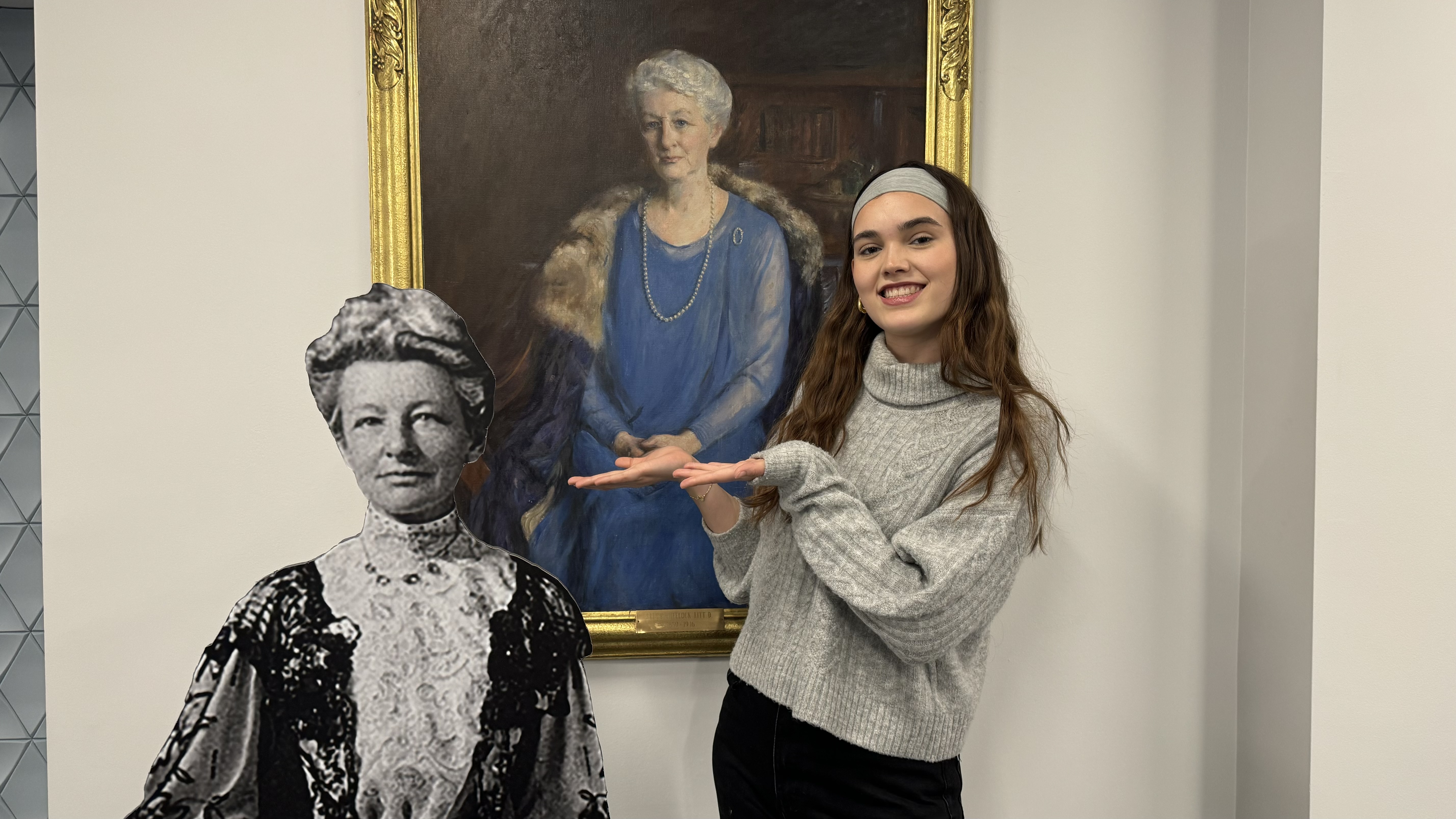 Female student smiling with black and white cutout of Lucy Wheelock infront of a portrait of Lucy Wheelock