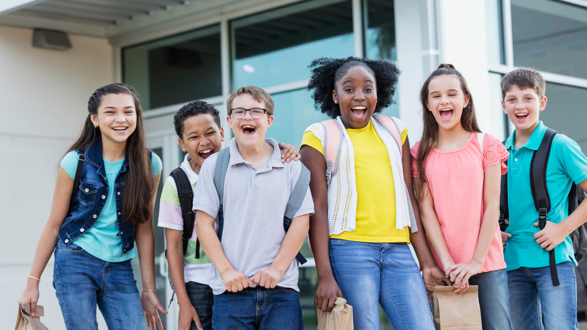 A group of middle school aged kids laughing and smiling outside of their school