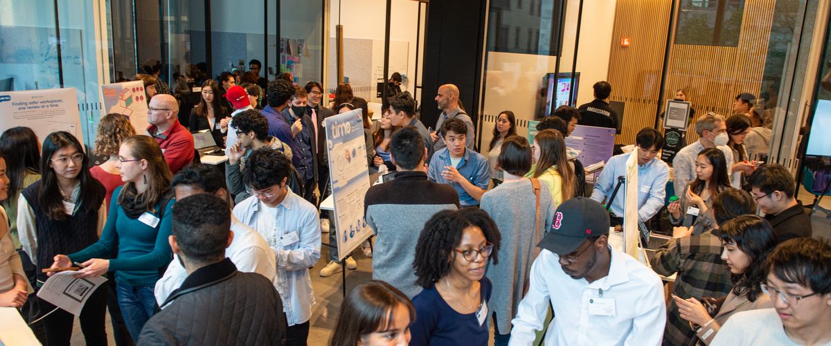 At the Boston University Learning Expo, students present their projects while teachers watch and evaluate. The room is busy and filled with learning and discovery.