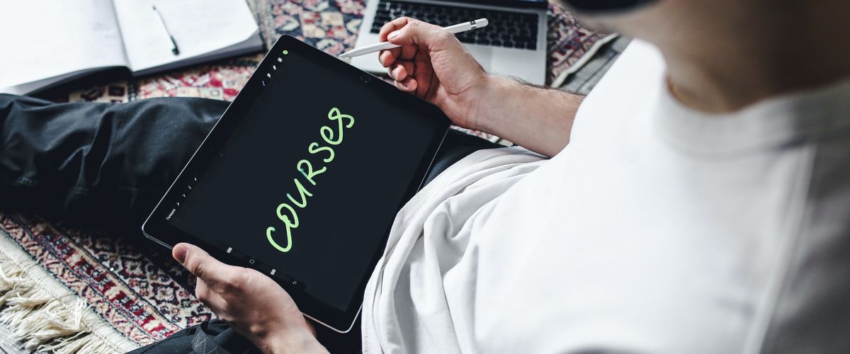 A guy sits on the floor, writing "Courses" on a tablet and listening to music.