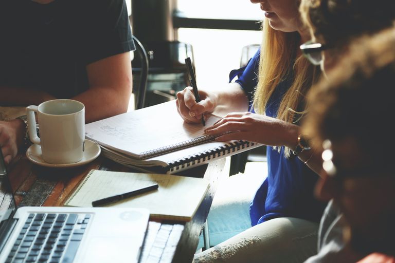 Four people sit around a table writing on notepads and a laptop.